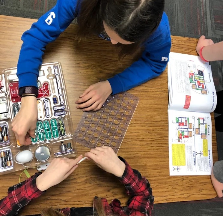 An overhead shot of three students working on assembling snap circuits at a table together.